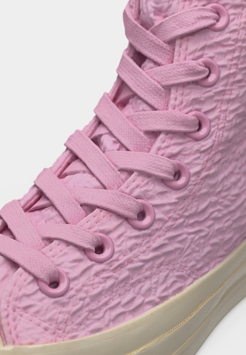 Primo piano di una sneaker alta rosa testurizzata con lacci rosa abbinati e suola in gomma beige.