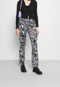 Svart ribbad långärmad topp med volangdetalj, kombinerad med högmidjade svarta och vita byxor med virvlande mönster och svarta snörboots.