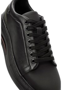 Sneaker in pelle nera con lacci neri piatti, occhielli in metallo, linguetta imbottita e suola in gomma testurizzata. Design elegante con accenti sottili.