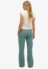 Crème ribbel top met korte mouwen en gegolfde randen, gecombineerd met teal uitlopende broek. Stof lijkt zacht; broek heeft zijzakken.