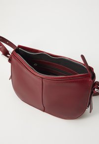Borsa a tracolla in pelle rossa con chiusura a zip, scomparti interni divisi e tracolla regolabile. Texture liscia senza pattern visibili.