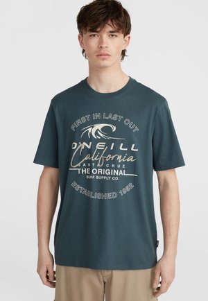 Camiseta de algodón de color verde azulado oscuro con mangas cortas, que presenta una impresión gráfica blanca de olas y texto. Cuello redondo y corte relajado.