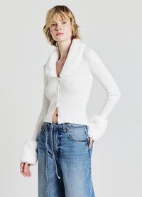 Cardigan bianco a coste con colletto e polsini in pelliccia sintetica, design corto, abbinato a jeans in denim blu larghi con cordoncino.