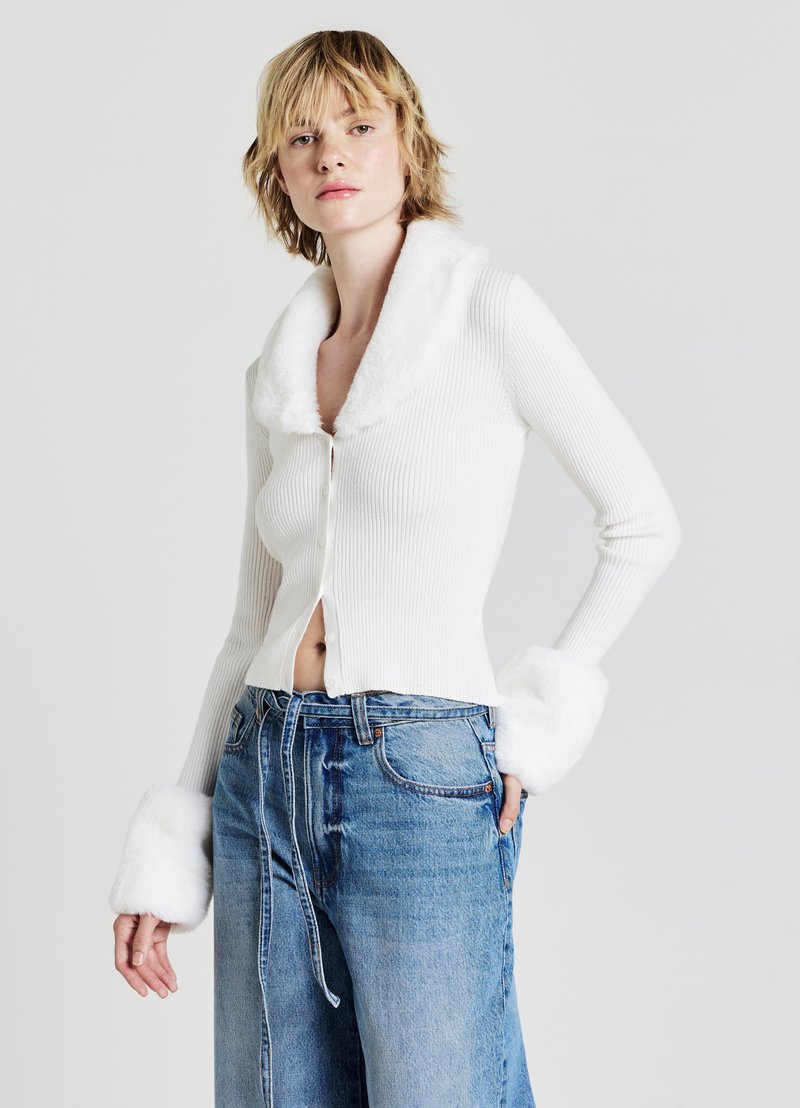 Cardigan bianco a coste con colletto e polsini in pelliccia sintetica, design corto, abbinato a jeans in denim blu larghi con cordoncino.