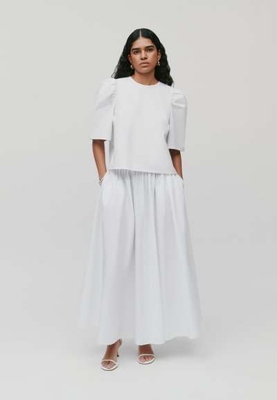 Witte outfit met een gestructureerde top met pofmouwen en een vloeiende, geraffineerde rok. Glad materiaal; minimalistisch ontwerp en silhouet.