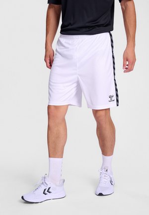 Hvide sportsshorts med sorte side-striber, elastisk talje, glat stof og logodetalje nær kanten. Båret med hvide sneakers.