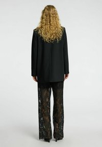 Mustat oversize-takit, joissa on muotoiltu istuvuus, yhdistettynä leveälahkeisiin mustiin pitsihousuihin, joissa on kukkakuosi ja läpinäkyviä kohtia.