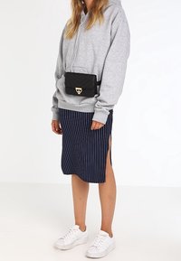 Felpa grigia, gonna midi a righe navy con spacchi laterali, borsa a tracolla nera trapuntata e sneakers bianche con suola testurizzata.