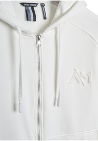 Felpa bianca con zip realizzata in tessuto morbido, dotata di un logo testurizzato sul petto, di lacci regolabili e di un design a vestibilità normale.