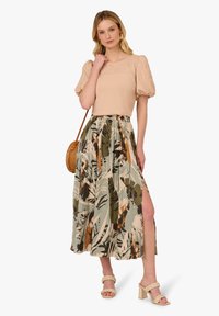 Top beige con maniche a sbuffo e dettagli floreali, abbinato a una gonna lunga e fluida con stampa di foglie verdi e arancioni e uno spacco alto fino alla coscia.