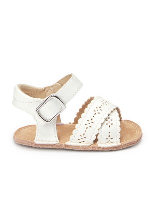 Sandale blanche pour tout-petit avec bords festonnés, brides à découpes florales, boucle de cheville réglable et semelle en daim beige.