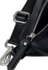 Close-up van een zwarte leren tas met een getextureerd oppervlak, zilver metalen hardware, rits en een afneembare schouderband met een clip.