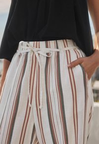 Lightweight linen pants with vertical stripes in beige, rust, and green hues. Features an adjustable white tie waist and side pockets.