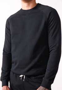 Schwarzer Rundhalsausschnitt-Pullover aus weichem Stoff, mit gerippten Bündchen und glatter Textur. Getragen mit passenden Hosen und Kordelzug.