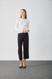 Haut à manches longues blanc côtelé avec des accents noirs, associé à un pantalon noir cropped et des talons noirs, sur fond uni.