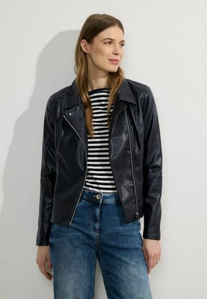 Veste de motard en cuir noir avec fermeture éclair, col cranté et manches longues, portée sur une chemise rayée noir et blanc et un jean en denim.
