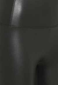 Černé legíny vyrobené z lesklého, elastického materiálu; hladká textura s vysokým pasem a bezešvým designem, obsahující jemné švy.