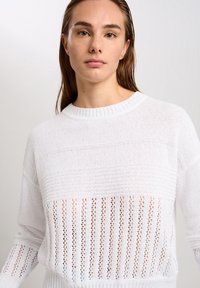 Weißer gestrickter Pullover mit einem strukturierten Muster aus horizontalen und vertikalen Streifen. Runder Halsausschnitt, lange Ärmel und offene Strickabschnitte.