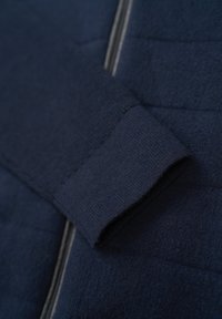 Nahaufnahme einer marineblauen Fleecejacke mit einem gerippten Bündchen und einem strukturierten Obermaterial mit Reißverschluss, das das weiche Material und die detaillierte Nahtführung betont.
