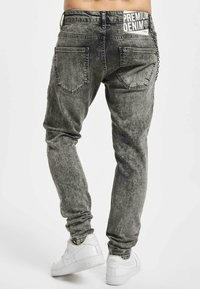 Jeans din denim gri cu o textură uzată, având cinci buzunare și un brâu cu marcă. Îmbunătățite cu un detaliu de lanț.