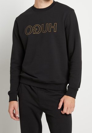 Sweatshirt noir avec un logo "HUGO" doré stylisé sur le devant. Design simple avec des poignets et un ourlet côtelés, fabriqué en tissu doux.