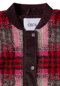 Col et devant d'une veste texturée à carreaux rouge, rose et marron, avec boutons-pression et étiquette "CECIL" à l'intérieur du col.