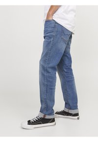 Jeans en denim bleu moyen, coupe décontractée avec ourlets retroussés. Dispose d'un design à cinq poches et de coutures contrastées. Porté avec des baskets noires.