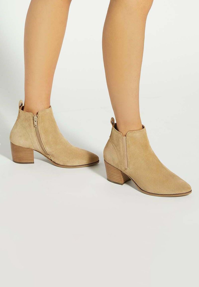 Beige suede ankle boots with a pointed toe, side zipper, and a stacked heel. Smooth texture with minimal stitching details.