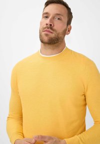 Gelb gestrickter Pullover mit Rundhalsausschnitt, strukturiertem Stoff und langen Ärmeln, ausgestattet mit einem gerippten Hals- und Ärmelbündchen.