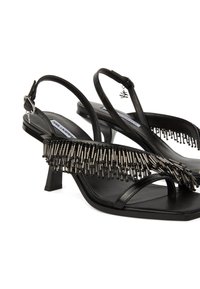 Melnas ādas sandales ar siksniņu, kurām ir metāliskas frizūras un zema papēža, ar vienkāršu siksniņu dizainu un gludu tekstūru.
