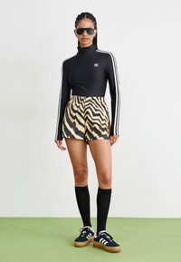 Μαύρη μπλούζα με μακριά μανίκια και λευκές ρίγες, κίτρινες βερμούδες με μαύρο zebra σχέδιο, μαύρες κάλτσες μέχρι το γόνατο και μαύρα αθλητικά παπούτσια.