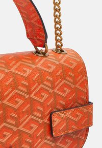 Sac à main rouge à motif géométrique, bandoulière chaîne dorée fixée par des œillets métalliques, avec un détail de poignée en tissu assorti.
