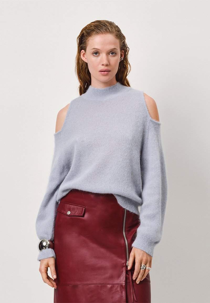 Lichtblauwe off-shoulder trui van zacht gebreide stof, gecombineerd met een bordeauxleren kokerrok met een zijrits en een drukknoopzak.