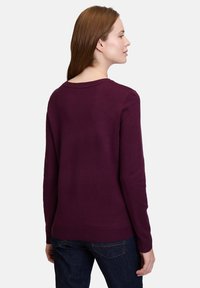 Maglione viola a maniche lunghe, collo rotondo, con polsini e orlo a costine, visto da dietro, abbinato a jeans in denim scuro.