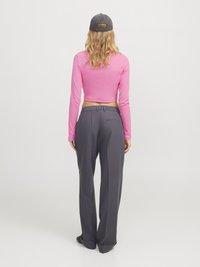 DugExtended pink crop top s dugim rukavima uparen s tamnosivim širokim hlačama. Model nosi sivi šešir, a vidljiva su mu valovita plava kosa.