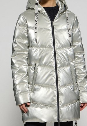Personne portant une doudoune argentée brillante avec une fermeture éclair à l'avant, des poches et le texte "POLO CLUB" sur les cordons blancs de la capuche.