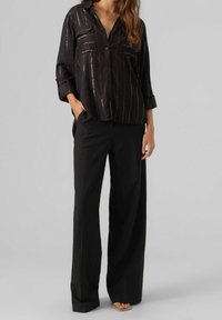 Black button-up shirt with metallic striped detailing and two chest pockets, paired with loose-fitting black trousers. Soft fabric texture.