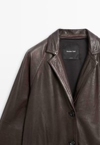 Bruine leren jas met een ingesneden kraag, knoopsluiting en een soepele textuur. Binnenlabel vermeldt "Massimo Dutti."