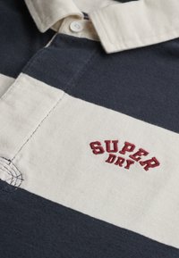 Polo shirt met een katoenmix, met marineblauwe en crèmekleurige horizontale strepen. Rood geborduurd "SUPER DRY" logo op de voorkant. Kraag met knopen.