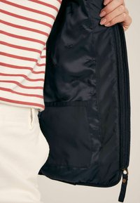 Tengeri kék steppelt dzseki bélése, kis zsebbel, sima anyagon megformált ló motívumokkal. A külső oldal nem látható.