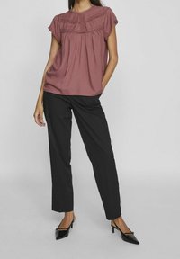 Blusa corta color ruggine con dettagli testurizzati, abbinata a pantaloni neri su misura e tacchi appuntiti neri.