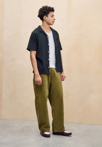 Maglietta nera a maniche corte, canotta grigia, pantaloni larghi verde oliva e scarpe marroni con dettagli bianchi. Design semplice, minimo uso di fantasie, vestibilità casual.