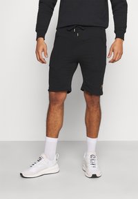 Black athletic shorts made of cotton blend, featuring an elastic waistband with drawstring and side pockets. Gold logo accent on leg.