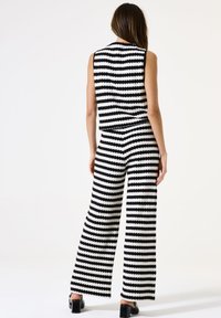 Top sin mangas de punto a rayas en blanco y negro y pantalones de pierna ancha con un acabado texturizado. El conjunto presenta patrones escallopados horizontales.