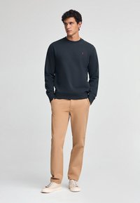 Sudadera de un oscuro azul marino en mezcla de algodón, con cuello redondo acanalado y puños. Combinada con chinos beige y zapatillas de color claro.