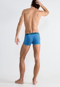 Blaue Herren-Boxershorts mit figurbetontem Design, aus glattem Material, mit einem schwarzen Bündchen mit Markenlogo und einer weichen Textur.