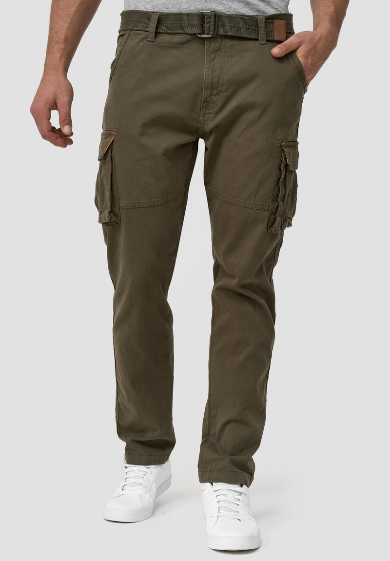 Pantalon cargo vert olive pour homme avec multiples poches, associé à des baskets blanches et une ceinture décontractée à la taille.