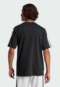 Černé bavlněné tričko s krátkým rukávem, kulatým výstřihem a bílými pruhy podél ramen; volný střih a hladká textury.