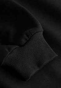 Gros plan d'une manche de sweat-shirt noire montrant un poignet côtelé et une texture de tissu lisse.