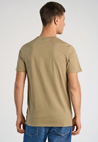 Khaki t-shirt z miękkiej bawełny z krótkimi rękawami, okrągłym dekoltem i luźnym krojem, zestawiona z niebieskimi dżinsami.